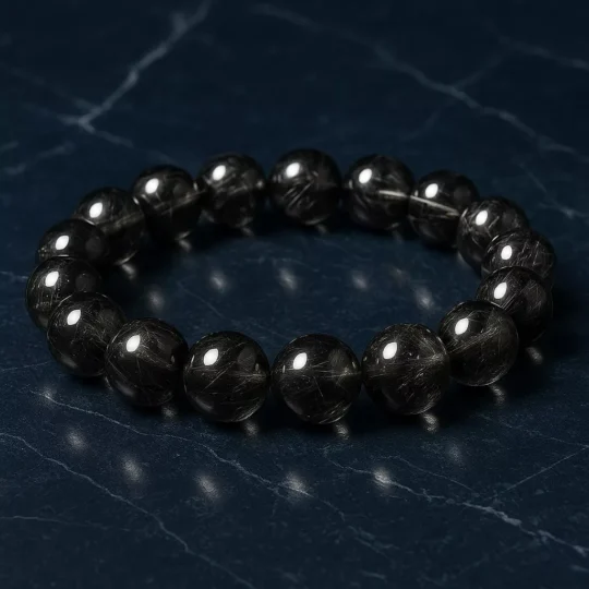 A black rutilated quartz bracelet with natural thread-like inclusions, resting on a textured stone background, symbolizing Water element flow