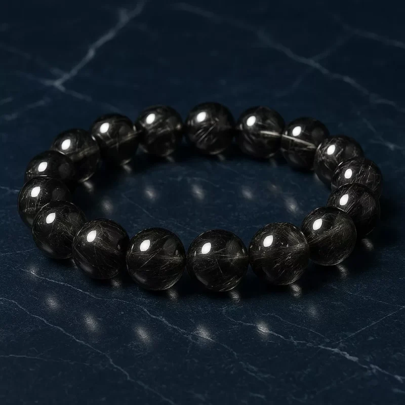 A black rutilated quartz bracelet with natural thread-like inclusions, resting on a textured stone background, symbolizing Water element flow
